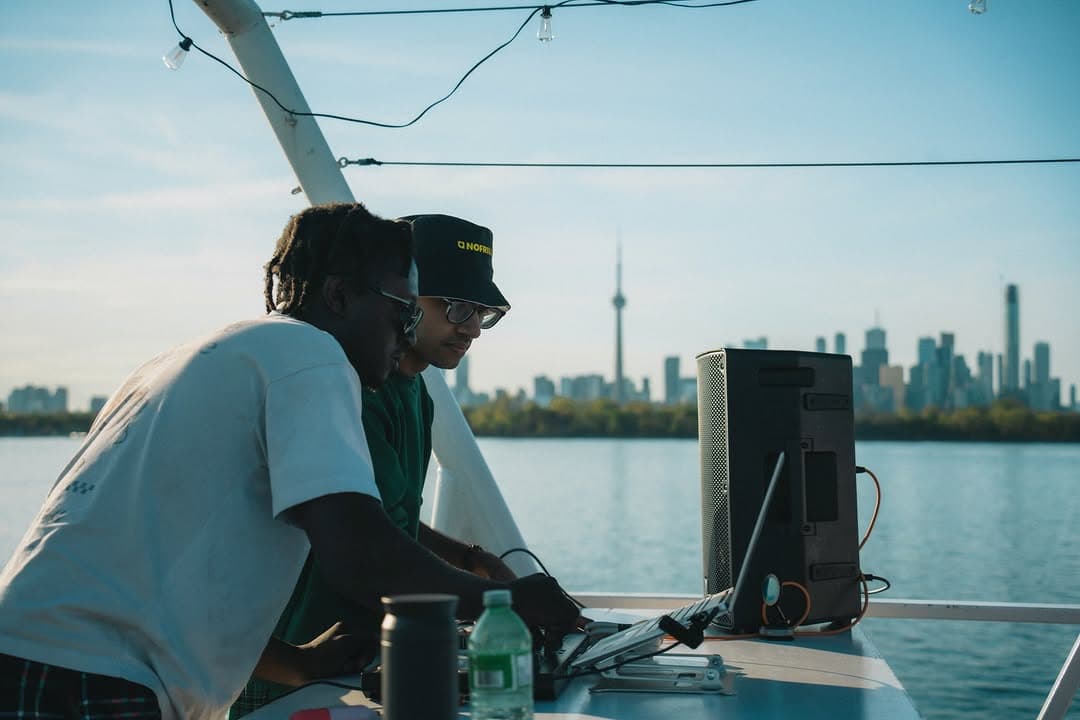 DJ playing on deck with speakers, open water and the skyline behind