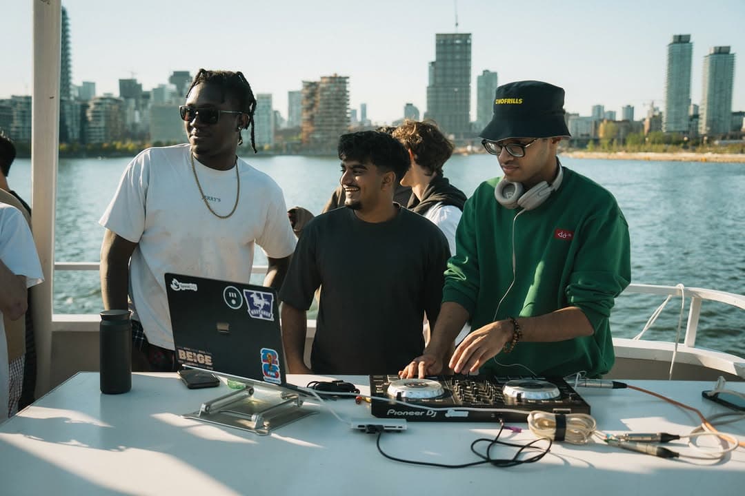 DJs behind a table of decks and laptops on the deck, the skyline behind them