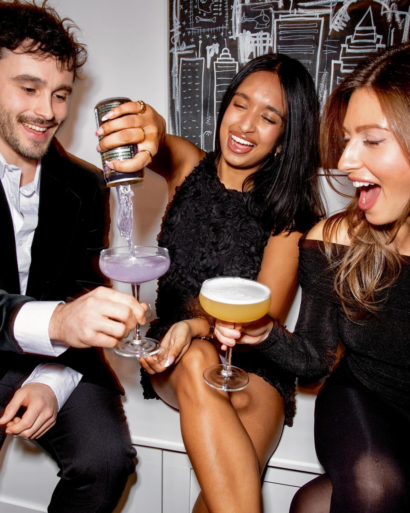 Guests laughing and toasting cocktails, caught on flash at the first event